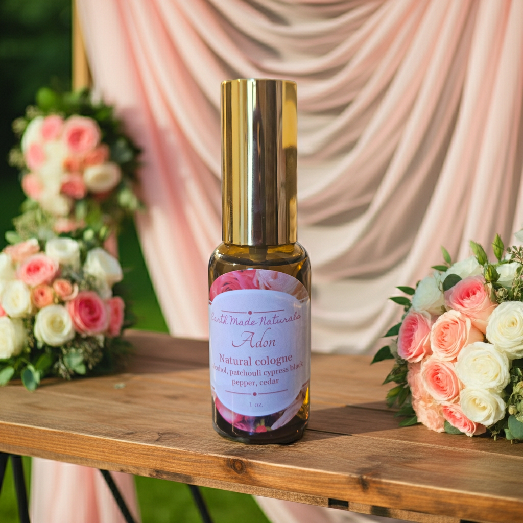 A bottle of Adon Natural Cologne placed on a wooden table, flanked by pink and white rose bouquets, with a draped pink fabric backdrop in the background.